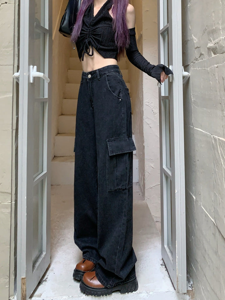 Une femme debout dans une porte avec un jean cargo large taille haute noir. Le jean a des poches latérales cargo pour une touche fonctionnelle. Disponible du S au XL.