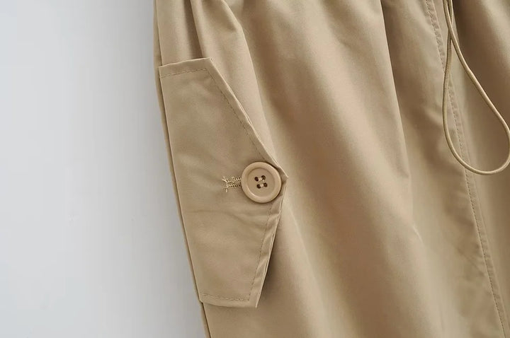 Une vue rapprochée d'une poche boutonnée sur une jupe cargo longue légère beige pour femme. Les détails utilitaires ajoutent une touche tendance aux années 2000.