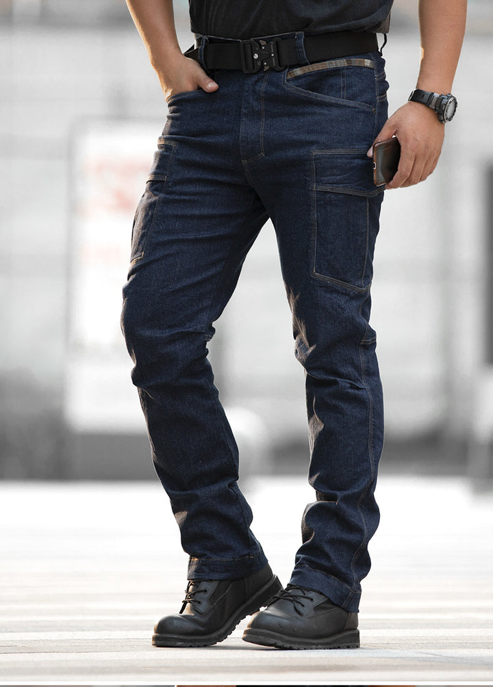 Un homme pose dans la rue avec un jean cargo ajusté coupe droite bleu, un tee-shirt et des boots noirs. Il a une ceinture et une montre noires et porte son téléphone à la main. 