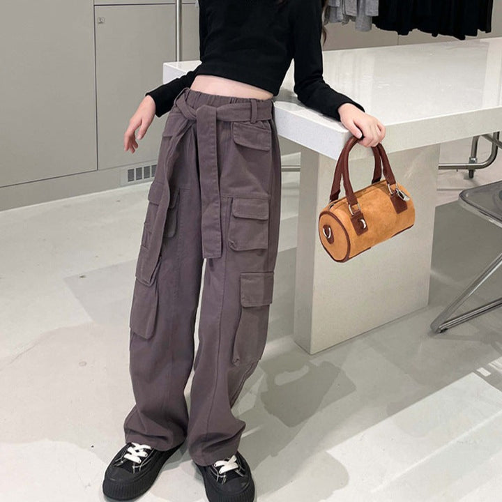 Une femme porte un Pantalon cargo large taille haute ceinture gris avec multiples poches latérales. Modèle confortable et à la mode pour petite fille. Disponible du 120 au 170 cm.