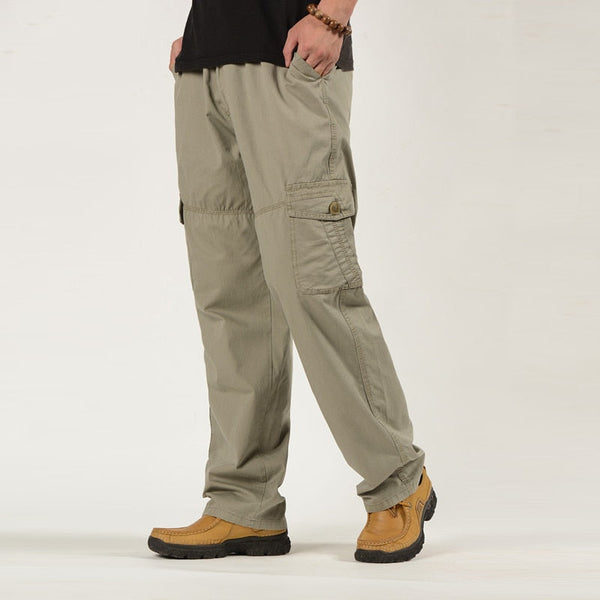 Un homme pose avec un tee-shirt noir, un pantalon cargo coupe droite ample de couleur beige. Il porte aussi des chaussures camel.