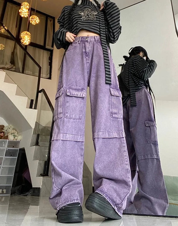 Une femme pose dans un tee shirt manches longues rayés, des chaussures noires et un pantalon jean violet baggy cargo taille haute.