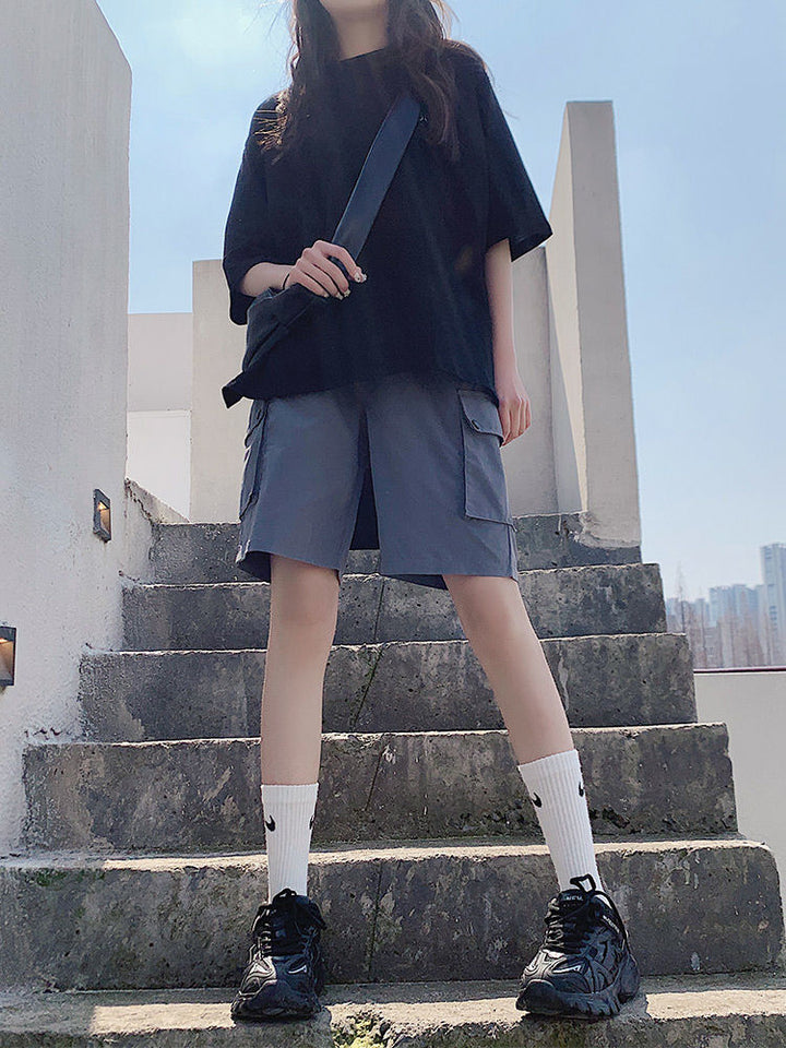 Une femme debout sur un escalier en béton, portant un Short cargo ample léger poches à clip - Gris - Femme de Cargo District.