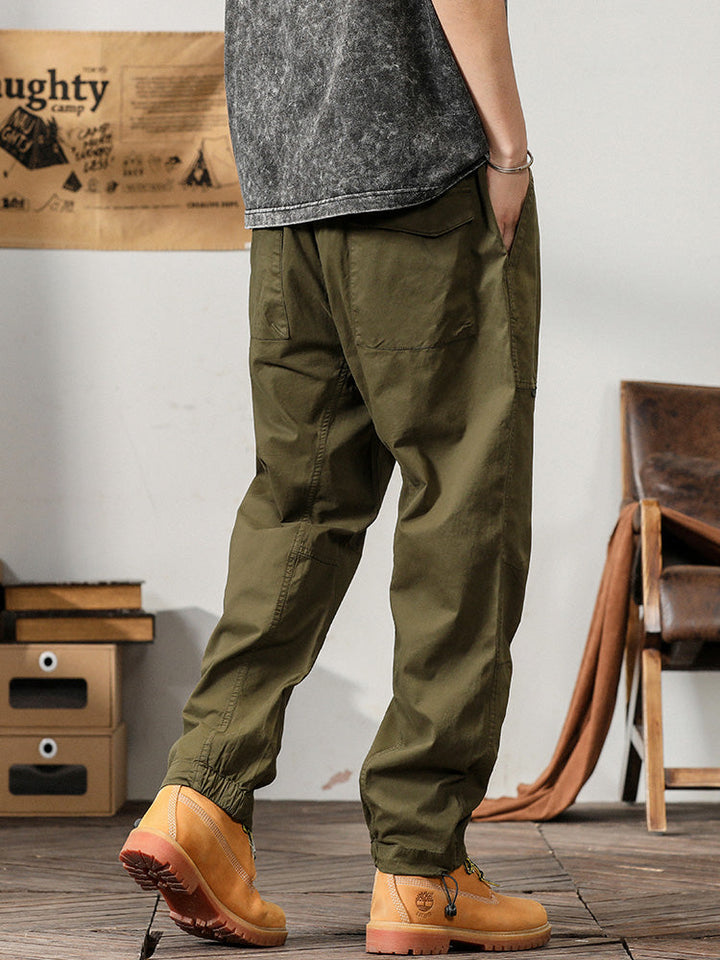 Un homme portant un pantalon cargo léger ample coupe droite kaki, parfait pour l'été. Doté de poches fonctionnelles sur les côtés, il offre confort et maintien grâce à l'élastique à la taille. Disponible du M au 3XL.