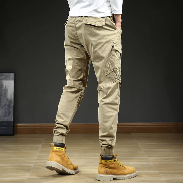 Un homme portant un pantalon cargo slim resserré aux chevilles, de couleur beige. Le pantalon est confortable et élégant, avec une coupe moderne et des coutures aux genoux. Disponible en tailles US 28 à 38.