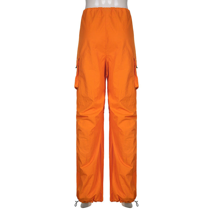 Une personne portant un pantalon orange cargo baggy taille basse pour femme de la marque Cargo District. Coupe large façon parachute avec lanières pendantes et chevilles élastiques. Disponible du S au L. Matières douces et extensibles pour un confort optimal.