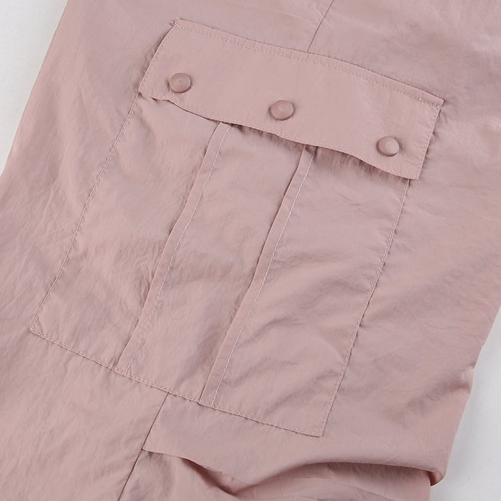 Un pantalon cargo rose avec une poche rapprochée et un bouton. Taille basse, style baggy, jambe large avec élastique à la cheville. Matière légère en polyester et spandex. Disponible du S au L. De Cargo District, site de vente de vêtements de style cargo.