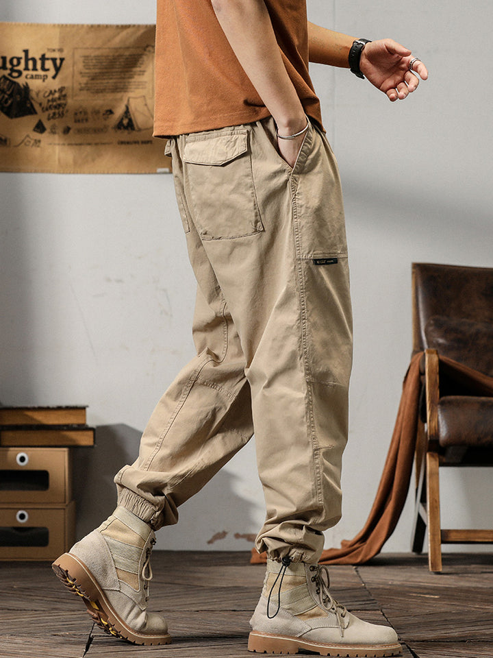 Un homme porte un pantalon cargo léger ample coupe droite beige. Les poches sur les côtés ajoutent une touche fonctionnelle. Tailles disponibles : M à 3XL.