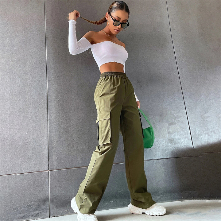 Une femme brune avec une tresse et des lunettes de soleil porte un top bustier à manches longues blancs, des baskets blanches, un sac vert et un pantalon cargo baggy vert kaki à taille élastique haute.  