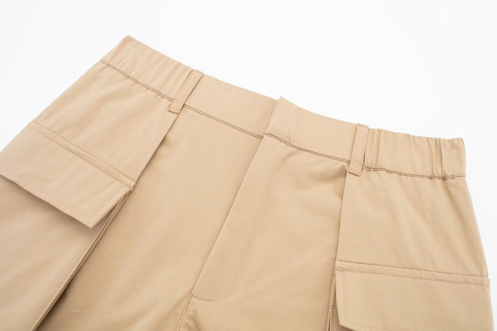 Une paire de pantalons cargo beige pour femme, avec une jupe courte à l'avant et un short à l'arrière. Tailles S à XL. Matières : polyester léger et durable. Poches cargo ajoutant une touche de style unique.