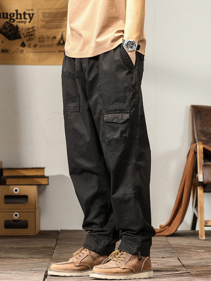 Un homme porte un pantalon cargo noir ample coupe droite. Le pantalon est léger et confortable avec des poches fonctionnelles sur les côtés. Disponible du M au 3XL.