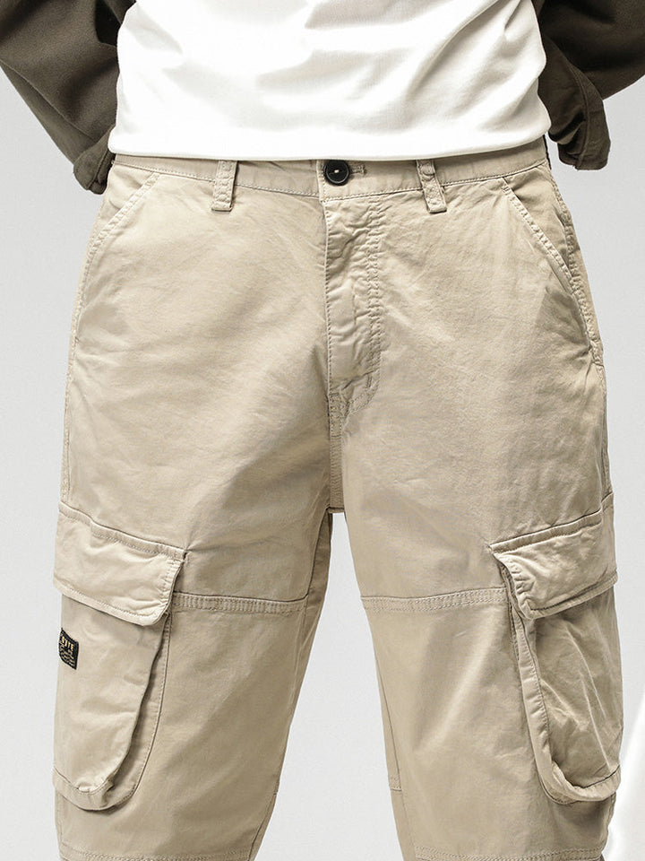 Un homme porte un pantalon cargo ample coupe droite beige avec des poches sur les côtés. Le pantalon est en coton et spandex, offrant confort et flexibilité.