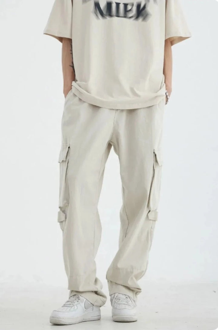Un homme portant un pantalon blanc cargo HOUZHOU pour homme, style safari décontracté, avec poches zippées. 100% coton. Tailles disponibles du M au 2XL.
