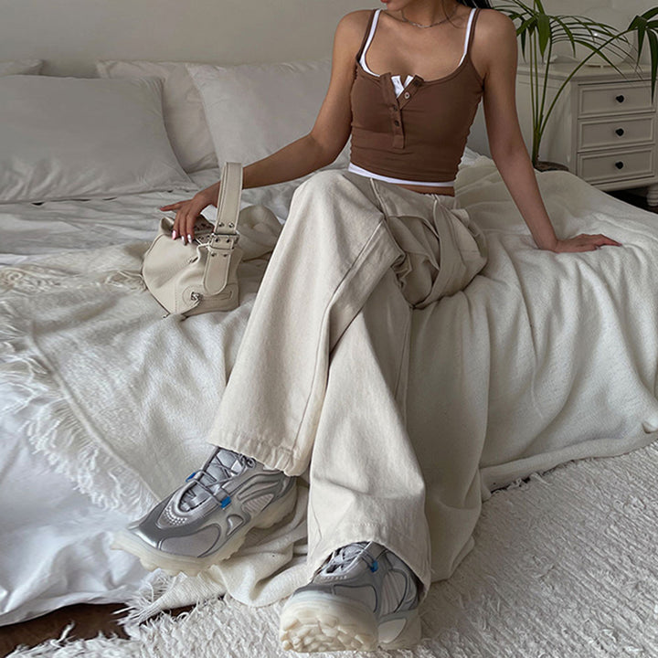 Une femme assise sur un lit, portant un jean cargo baggy taille haute élastique beige. Le jean est parfaitement ajusté grâce à son élastique à la taille et offre un confort inégalé. Les poches cargo latérales ajoutent une touche streetwear. Disponible du S au L.