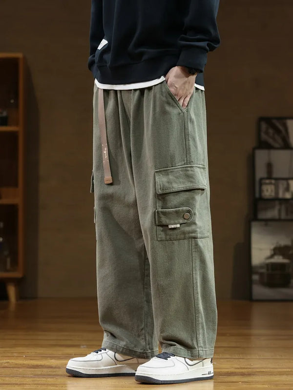 Un homme portant un pantalon cargo noir ample en coton. Ce pantalon résistant offre une liberté de mouvement optimale grâce à sa coupe ample. La ceinture intégrée ajoute une touche utilitaire chic. Disponible dans une gamme de tailles allant du M (FR36) au 8XL (FR56).