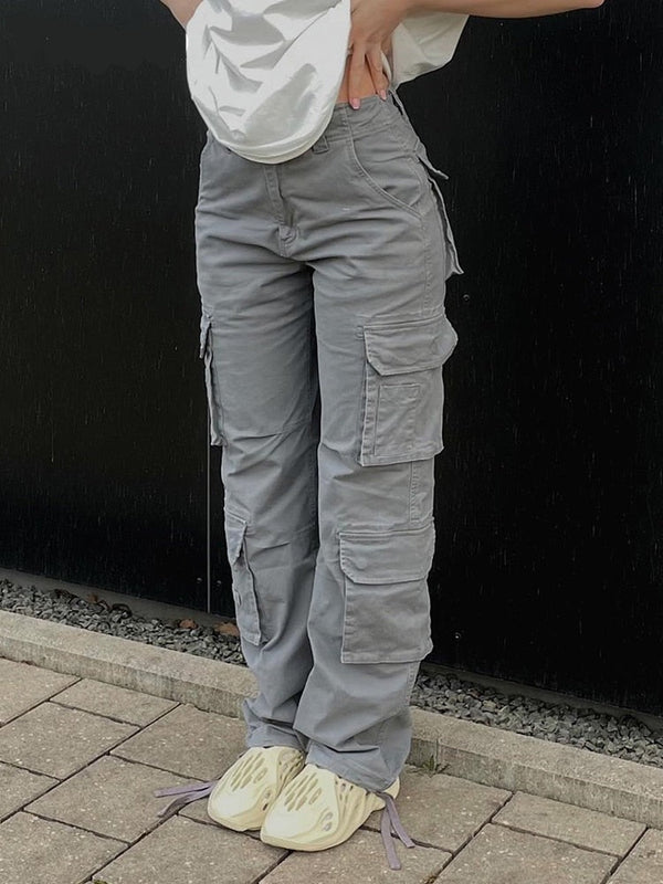 Une femme pose dans la rue avec un tee-shirt blanc, des baskets et un pantalon cargo coupe droite multipoches gris. 