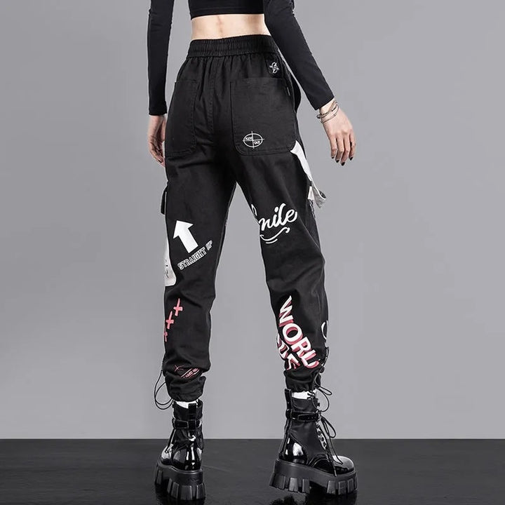 Une femme portant un pantalon cargo jogger noir à motifs avec une poche latérale et une lanière gris clair. Disponible du S au 3XL, ce pantalon cargo en coton offre un confort optimal pour un style urbain.