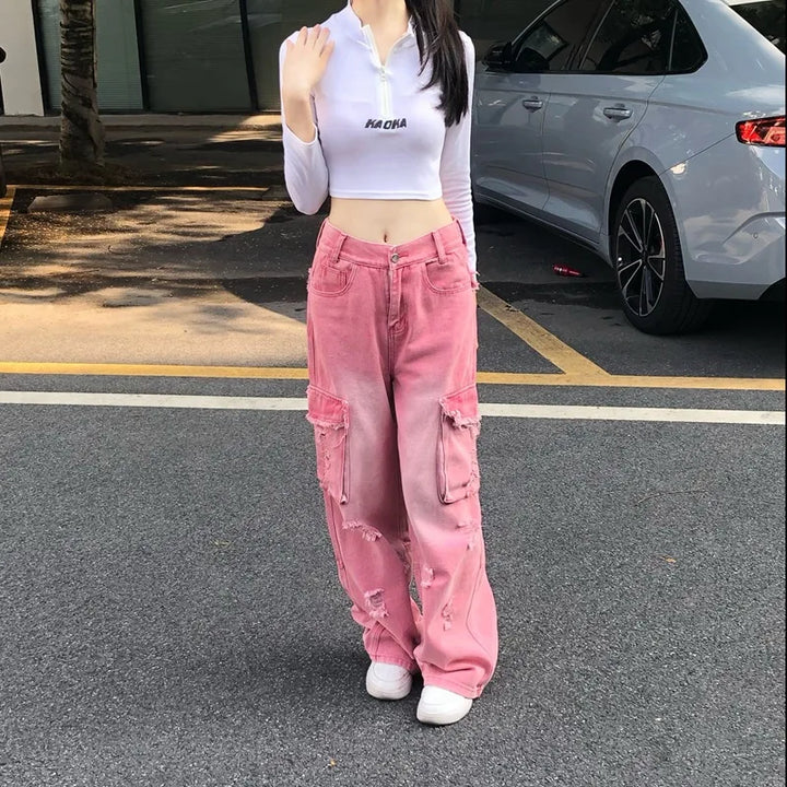 Une femme pose dans la rue avec un crop top blanc et un jean taille haute baggy cargo rose. Le jean est déchiré à certains endroits.