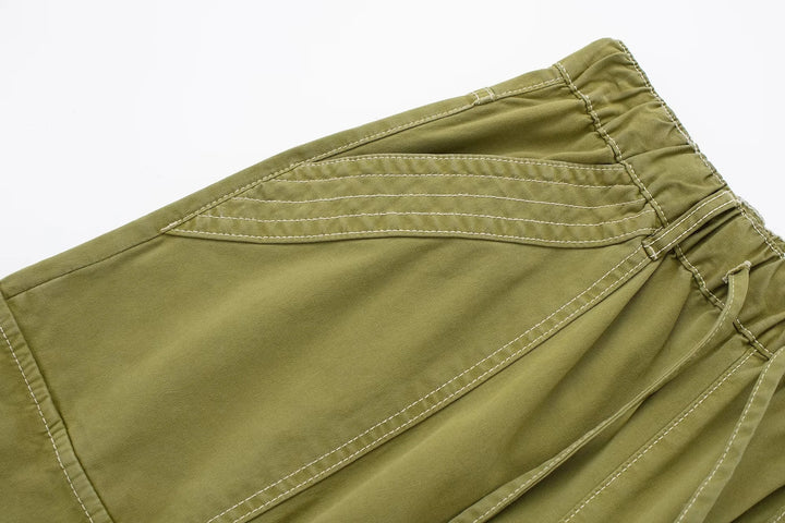 Un pantalon cargo vert avec coutures blanches, pour un look urbain féminin. Jambe large ajustable, taille haute ou basse. Disponible du XS au L.