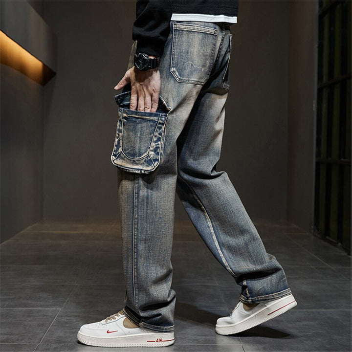 Un homme portant un jean cargo délavé coupe large - Bleu, avec une main dans la poche et une montre. Le jean offre un confort optimal et un style urbain et masculin avec ses poches latérales typiques du design cargo. Disponible en plusieurs tailles.