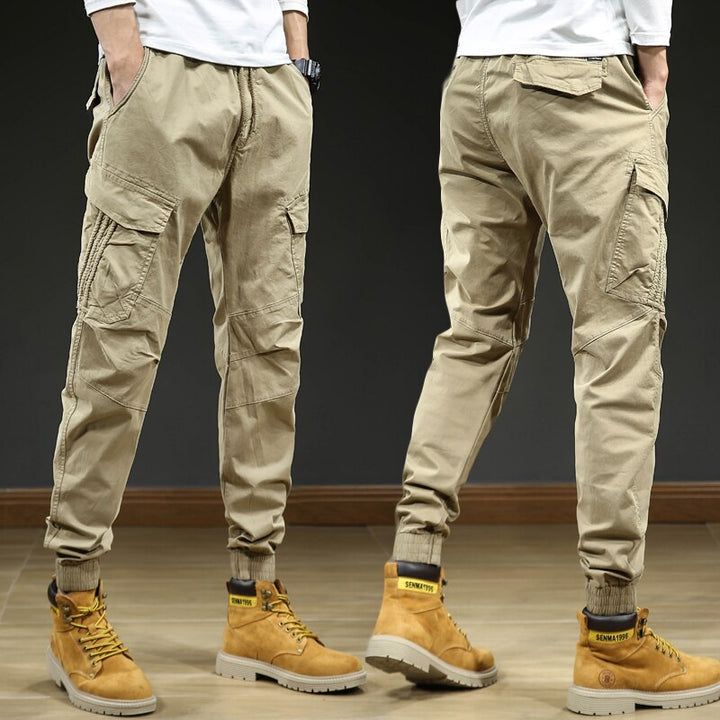 Un homme portant un pantalon cargo slim beige avec des chevilles resserrées. Le pantalon est confortable et élégant, avec une coupe moderne et des coutures aux genoux. Disponible en tailles US 28 à 38.