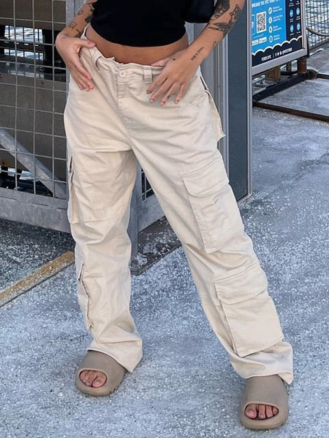 Une femme pose dans la rue avec un tee-shirt et sac noirs ainsi que des sandales taupe. Elle porte aussi un pantalon cargo coupe droite beige avec de nombreuses poches. 