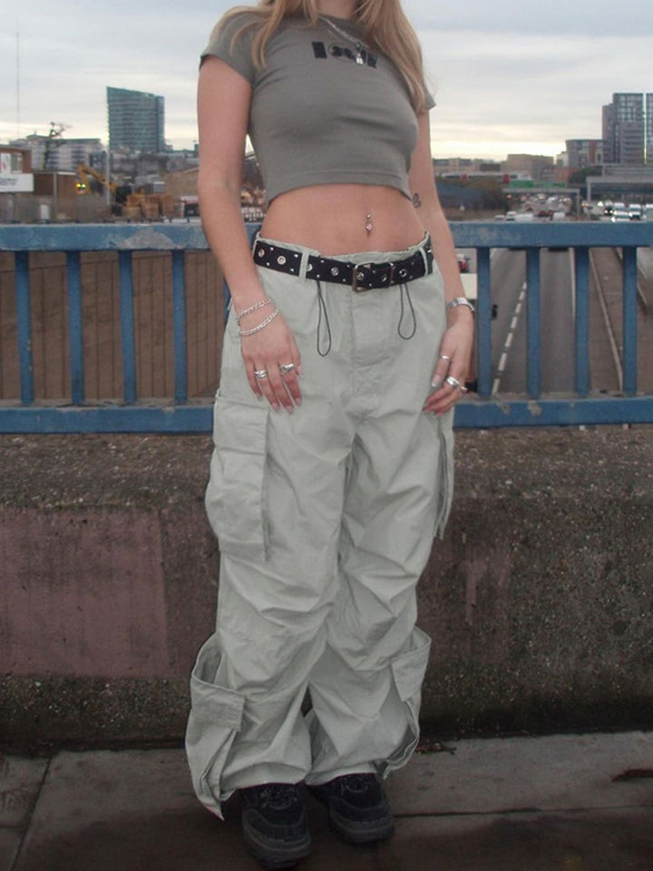 Une femme debout sur un pont, portant un Pantalon cargo large taille basse gris. Style urbain et baggy, disponible du S au L. Taille basse et élastique à la cheville pour personnaliser la forme. Poches latérales spacieuses ajoutant une touche de tendance et de fonctionnalité.