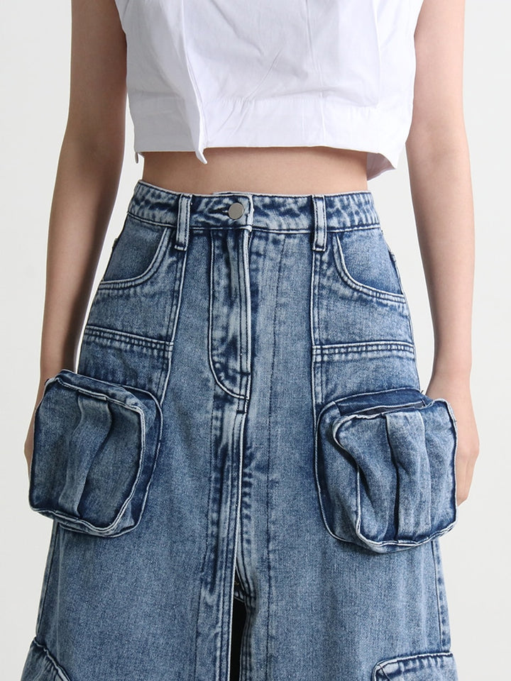 Une femme porte une jupe jean longue fendue multipoches bleue. Le design évasé et la fente offrent confort et liberté de mouvement. Les nombreuses poches ajoutent une touche fonctionnelle à cette jupe cargo taille haute. Disponible en tailles S à XL.