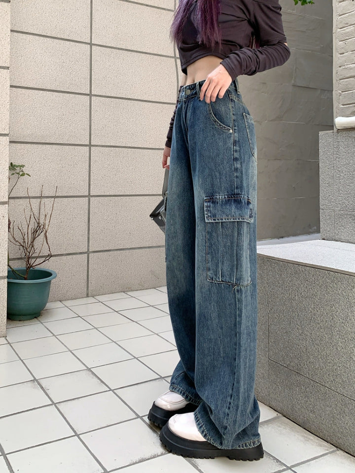 Une personne portant un crop top et un jean cargo large taille haute bleu, avec des poches cargo latérales fonctionnelles. Le jean est disponible du S au XL et est fait de denim et de polyester. Un choix tendance pour une garde-robe urbaine unique.