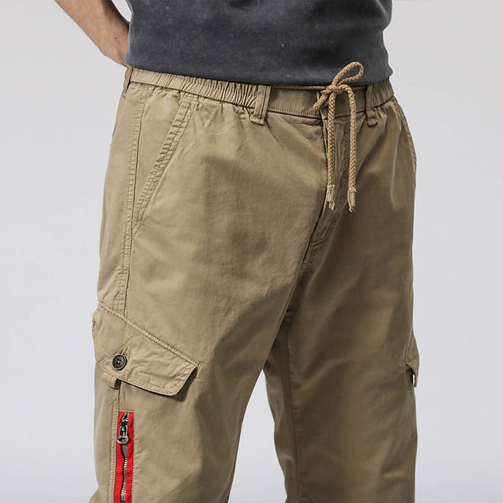 Un homme portant un pantalon cargo coupe droite avec fermeture rouge, couleur vert olive. Le pantalon est en coton et Spandex, offrant douceur, résistance et souplesse. Disponible dans les tailles 28 à 38 (US).