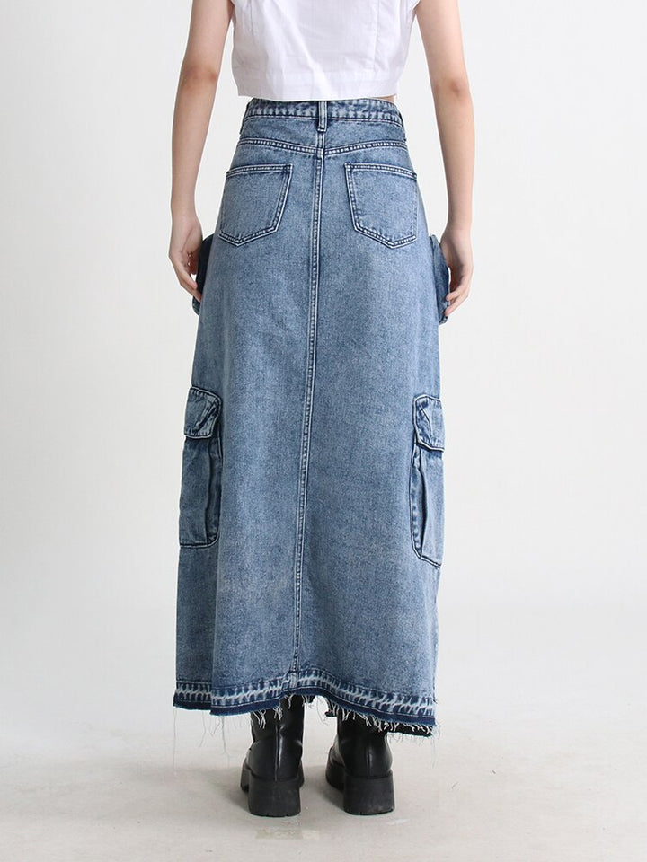 Une femme portant une jupe jean longue fendue multipoches bleue, ajoutant une touche urbaine et tendance à son style. La jupe cargo taille haute offre confort et liberté de mouvement grâce à son design évasé et sa fente. Les nombreuses poches ajoutent une touche de fonctionnalité à son allure féminine. Disponible en tailles S à XL.