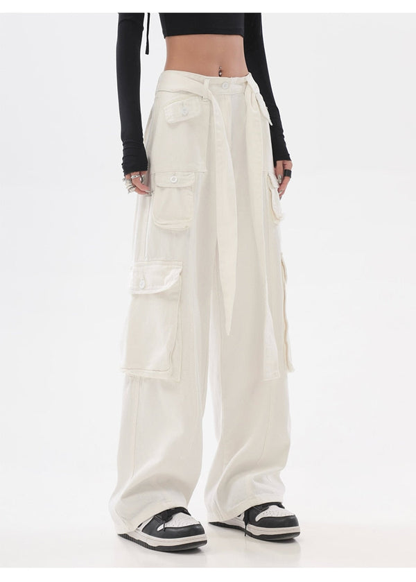 Une femme pose en top court noir, pantalon cargo taille haute baggy multipoches blanc avec ceinture à la taille. Elle porte aussi des baskets noires blanches.