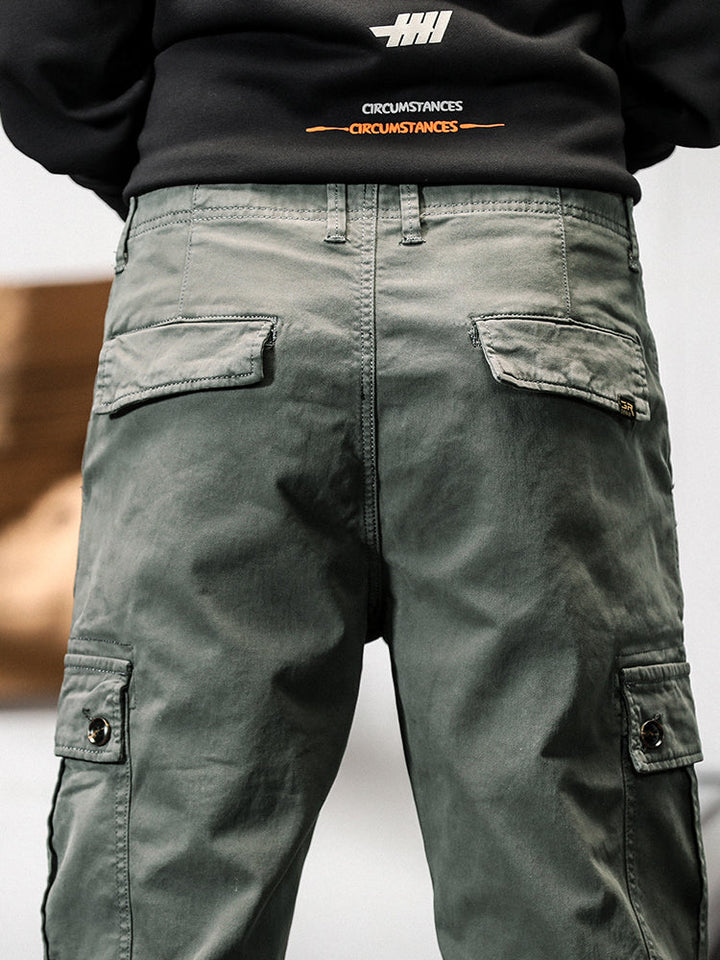 Un homme porte un pantalon cargo gris avec des poches cargo sur les côtés. Coupe droite, confortable et stylé. Disponible en tailles US 28 à 38.