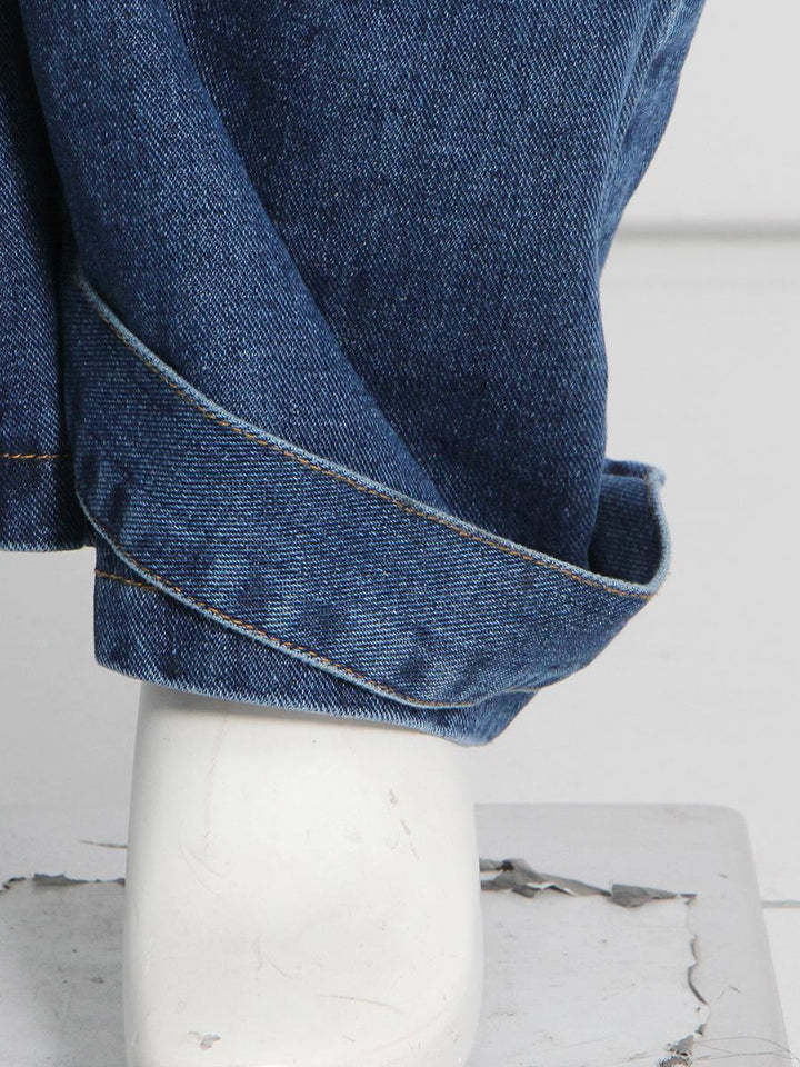 Un gros plan sur une jambe de jean cargo baggy taille basse pour femme, de couleur bleue. Les jambes larges et évasées ainsi que les nombreuses poches cargo lui confèrent un look unique et audacieux, parfait pour les amatrices de mode urbaine. Disponible du S au 2XL.