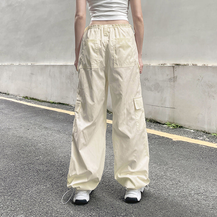 Une personne porte un Pantalon cargo baggy taille basse élastique blanc cassé pour femme. Le pantalon est en polyester et spandex, avec une coupe tendance et confortable grâce à l'élastique à la taille et aux chevilles. Disponible du S au L.