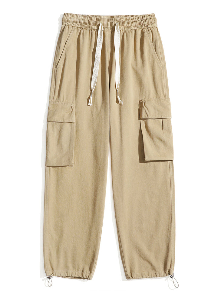 Un pantalon cargo baggy en coton beige pour homme avec poches. Coupe ample et confortable avec élastique à la taille et cordon de serrage. Élastique aux chevilles pour ajuster le style. Disponible du S au 2XL.