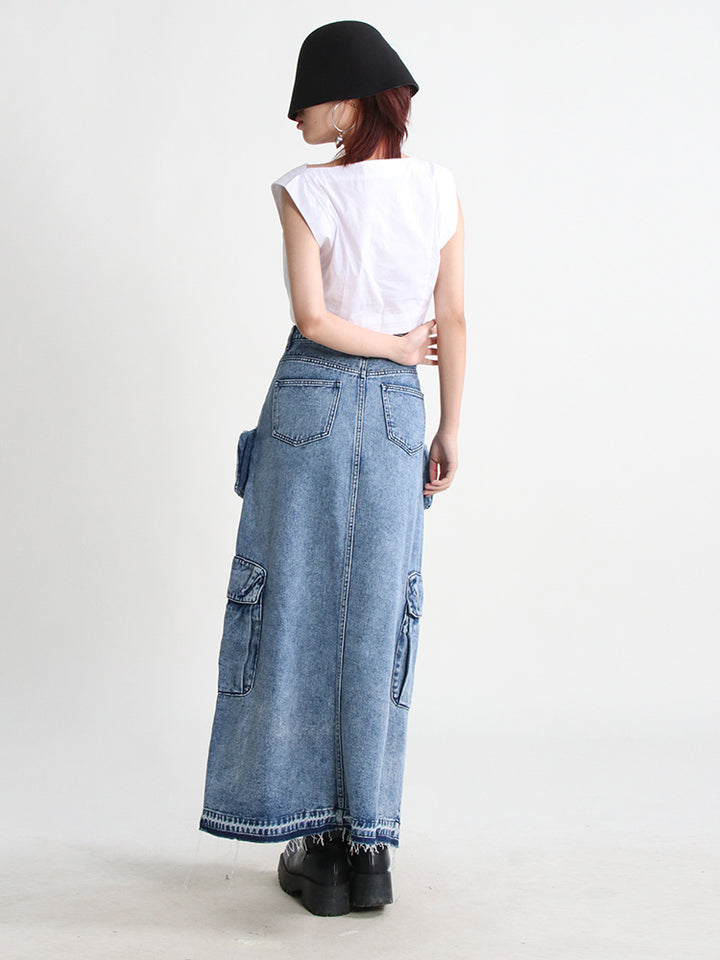 Une femme portant une jupe jean longue fendue multipoches bleue de style cargo. La jupe est taille haute et évasée, offrant confort et liberté de mouvement. Les nombreuses poches ajoutent une touche de fonctionnalité. Disponible en tailles S à XL.