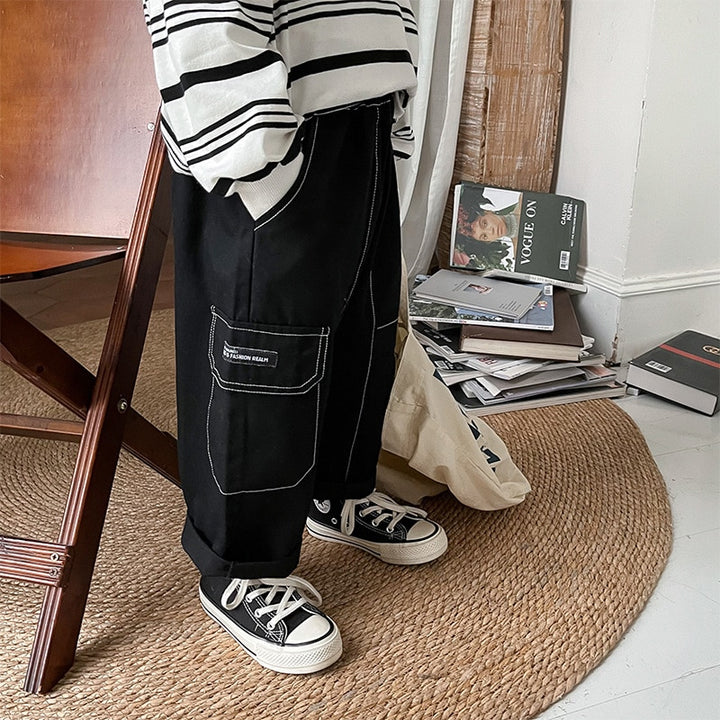 Un garçon à la mode debout près d'une chaise avec un pantalon cargo ample noir à coutures blanches.