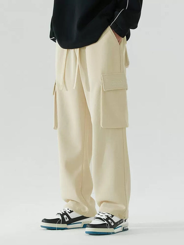 Un homme porte un pantalon cargo baggy blanc crème, pull noir et baskets blanches et noires.