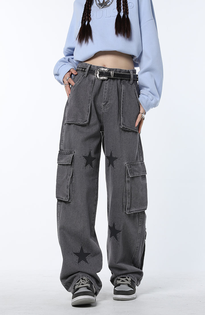 Une femme porte un jean cargo baggy gris avec des étoiles noires. Coupe confortable avec multiples poches pratiques. Look streetwear chic et féminin. Disponible du S au L.