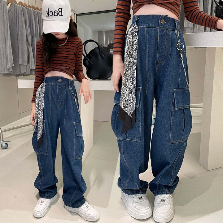 Deux filles portant un pantalon cargo jean avec foulard et chaîne - Bleu - Fille. Coupe ample, taille haute, poches latérales. Disponible du 4 au 14 ans. Modèle de style cargo typique pour exprimer sa personnalité avec glamour.