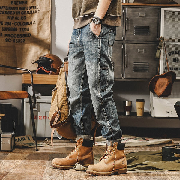 Un homme pose dans un décor industriel. Il porte un sweat taupe, des boots camel et un jean cargo délavé coupe droite.