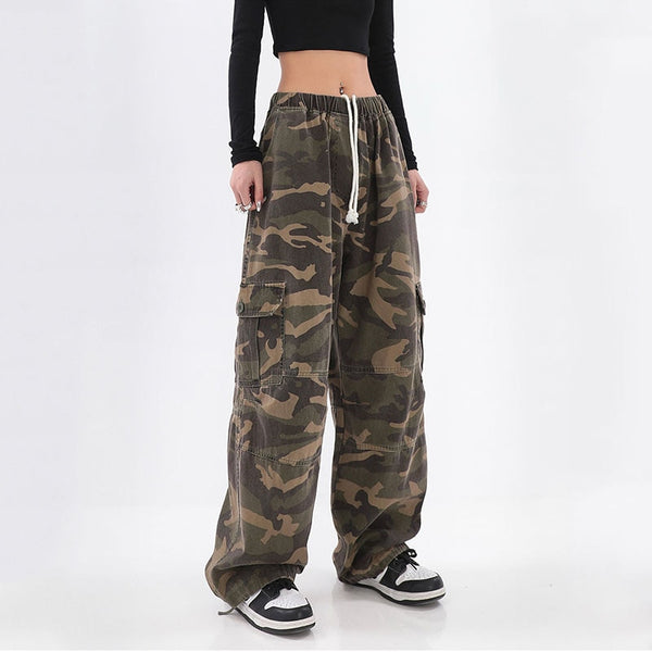 Une femme porte un top court manches longues noir avec des baskets noires et blanches et un pantalon cargo baggy camo vert kaki. 